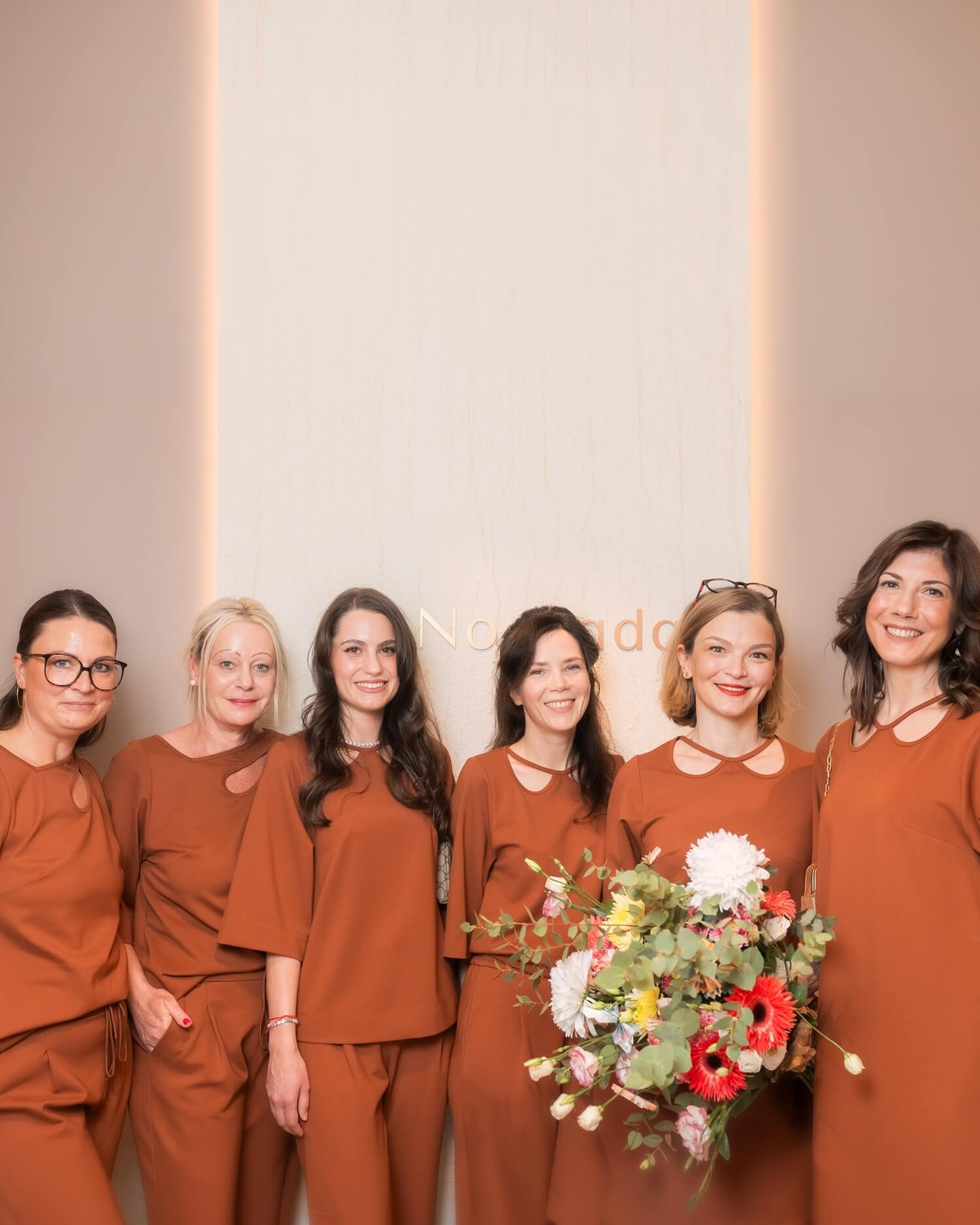 Sechs Dermatologinnen der Privatpraxis Nouvada in Trier stehen in stilvollen Arztkitteln nebeneinander.